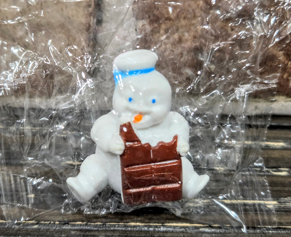 White mini Puft figure holding a brown chocolate bar, wearing a striped hat.