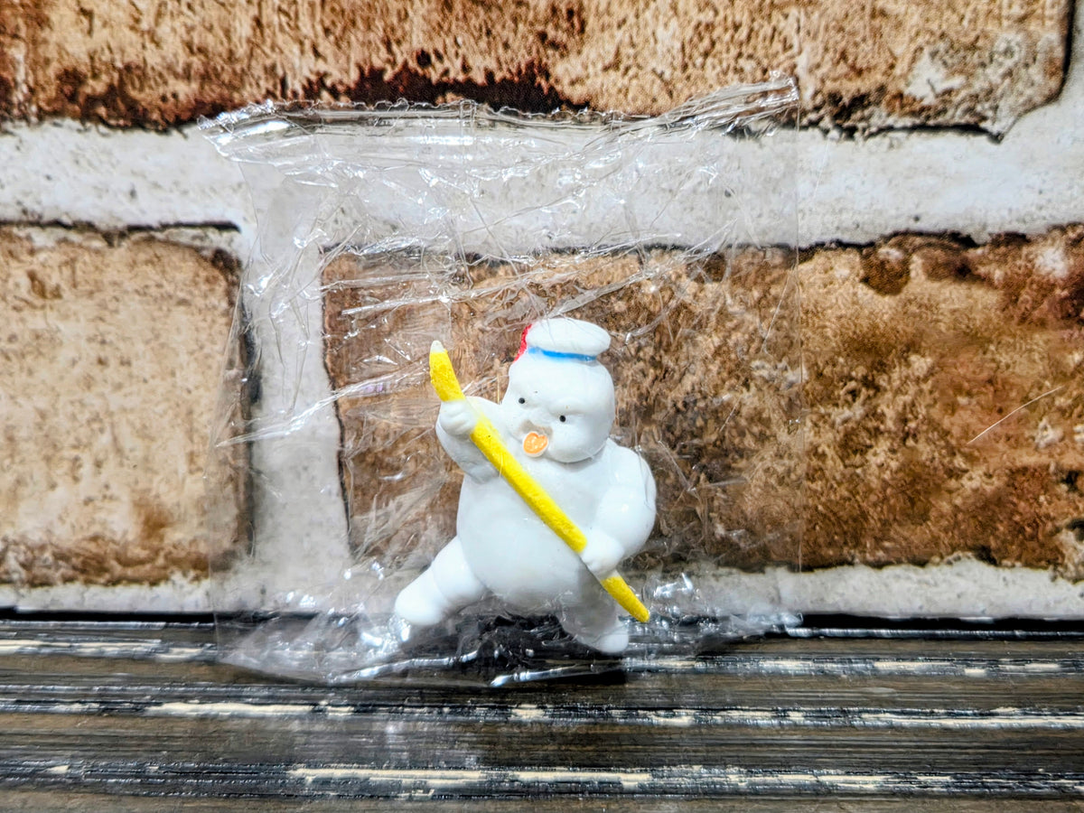 White mini figure with blue bib, holding yellow wand, standing in clear packaging