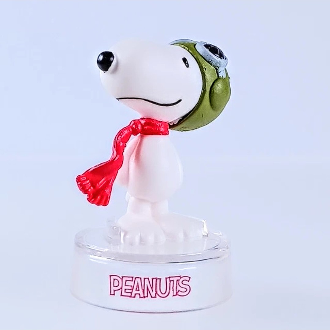 Snoopy figure with green face and red scarf, standing on clear PEANUTS base