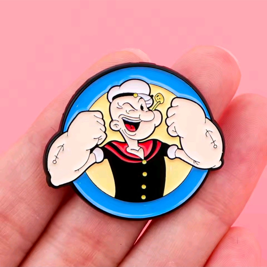 Cartoon sailor face enamel lapel pin, bold blue circle with raised fists and grin.