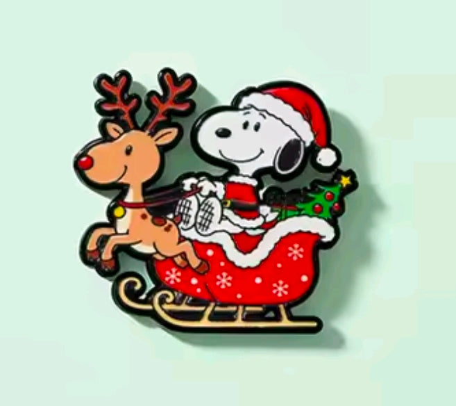 Snoopy and reindeer enamel pin in Santa outfit, seated on sleigh