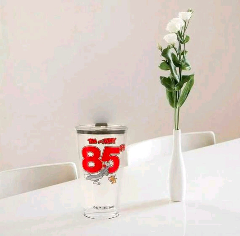 Clear glass tumbler with black lid and Tom & Jerry 85 graphic