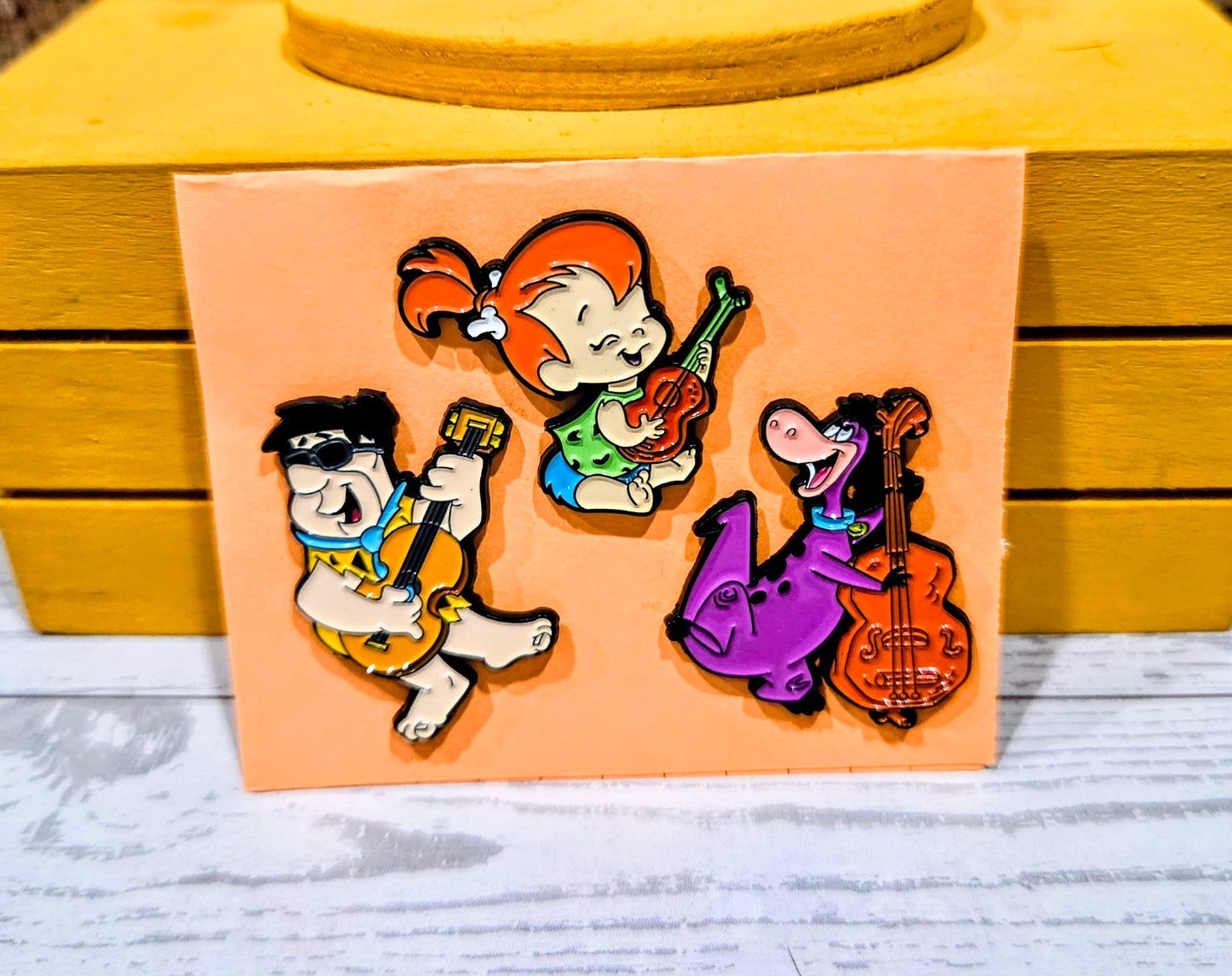 Enamel pin set featuring Fred, Pebbles, and Dino playing instruments on card