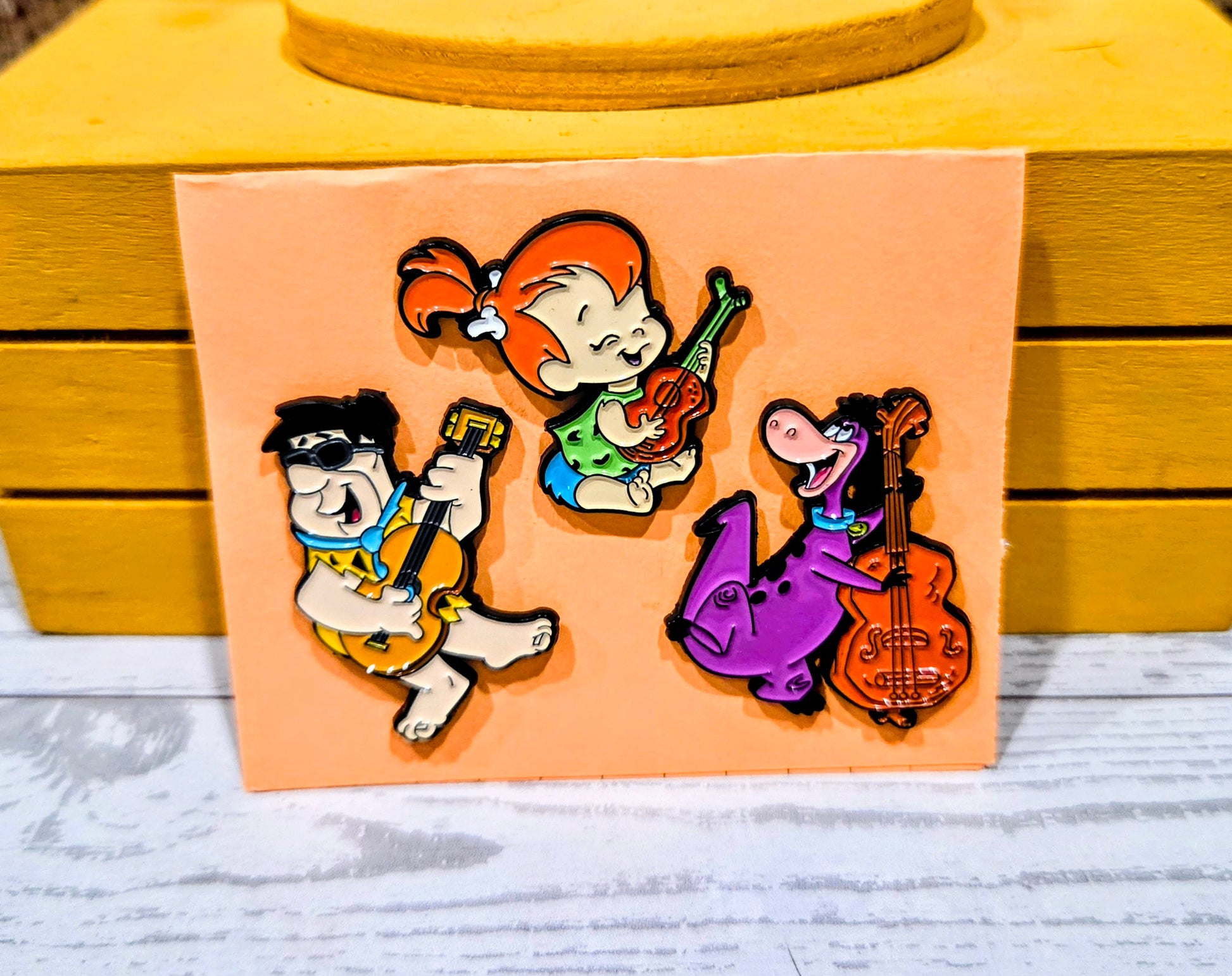 Enamel pin set featuring Fred, Pebbles, and Dino playing instruments on card