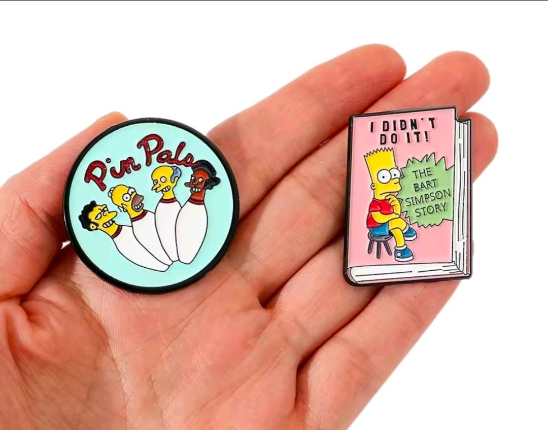 Simpsons enamel pin set with round turquoise Pin Pals pin and pink book-shaped pin