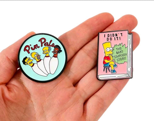 Simpsons enamel pin set with round turquoise Pin Pals pin and pink book-shaped pin