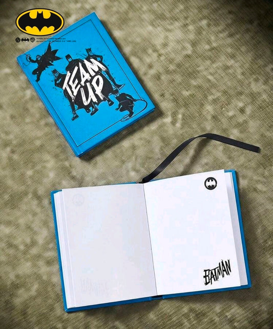 Open blue hardcover journal with blank white pages and Batman emblem