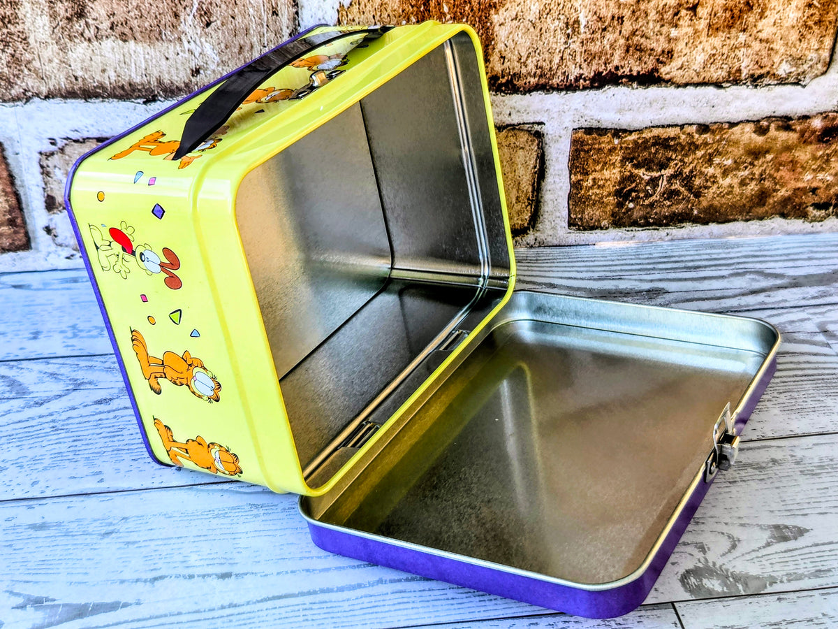 Open yellow and purple Garfield pet tin container with silver metal interior.