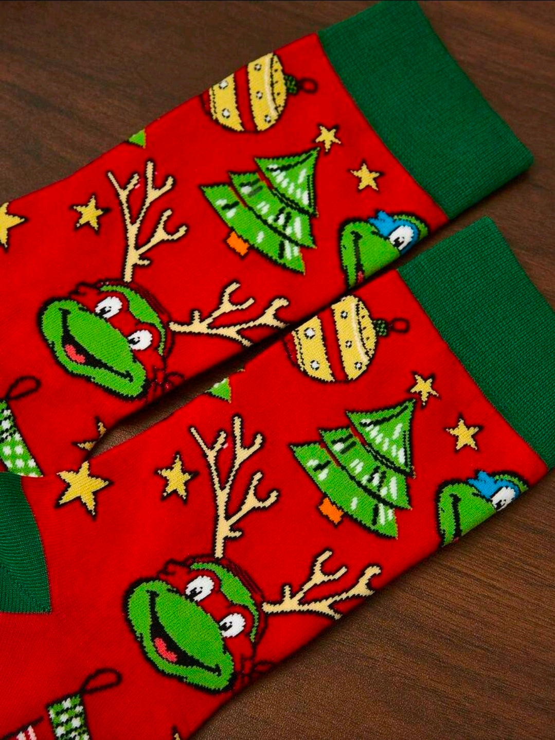 Red crew socks with green cuffs and cartoon turtle holiday print, laid on wood