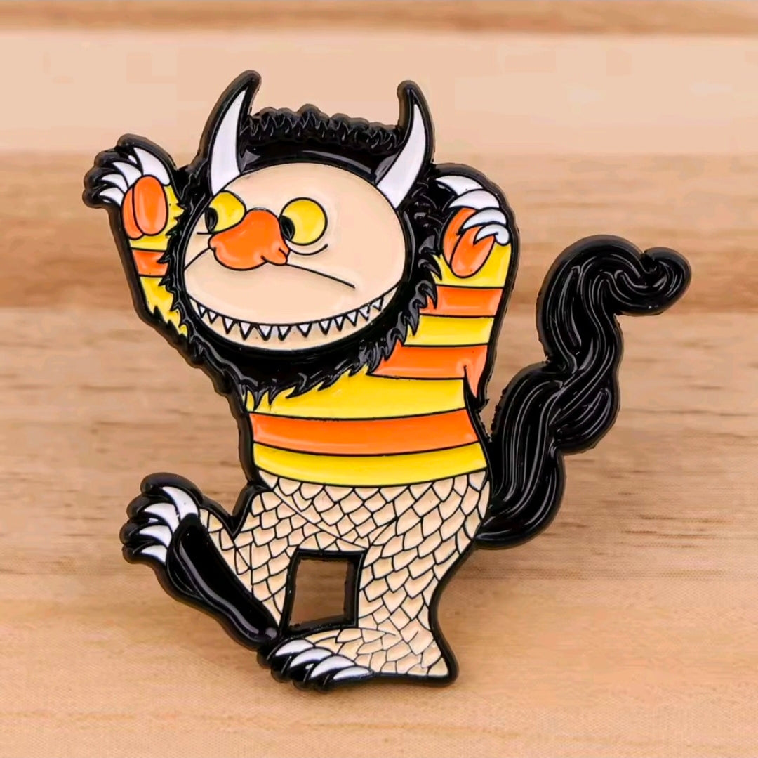 Enamel pin: wild thing creature with orange stripes and scaly body on wood surface