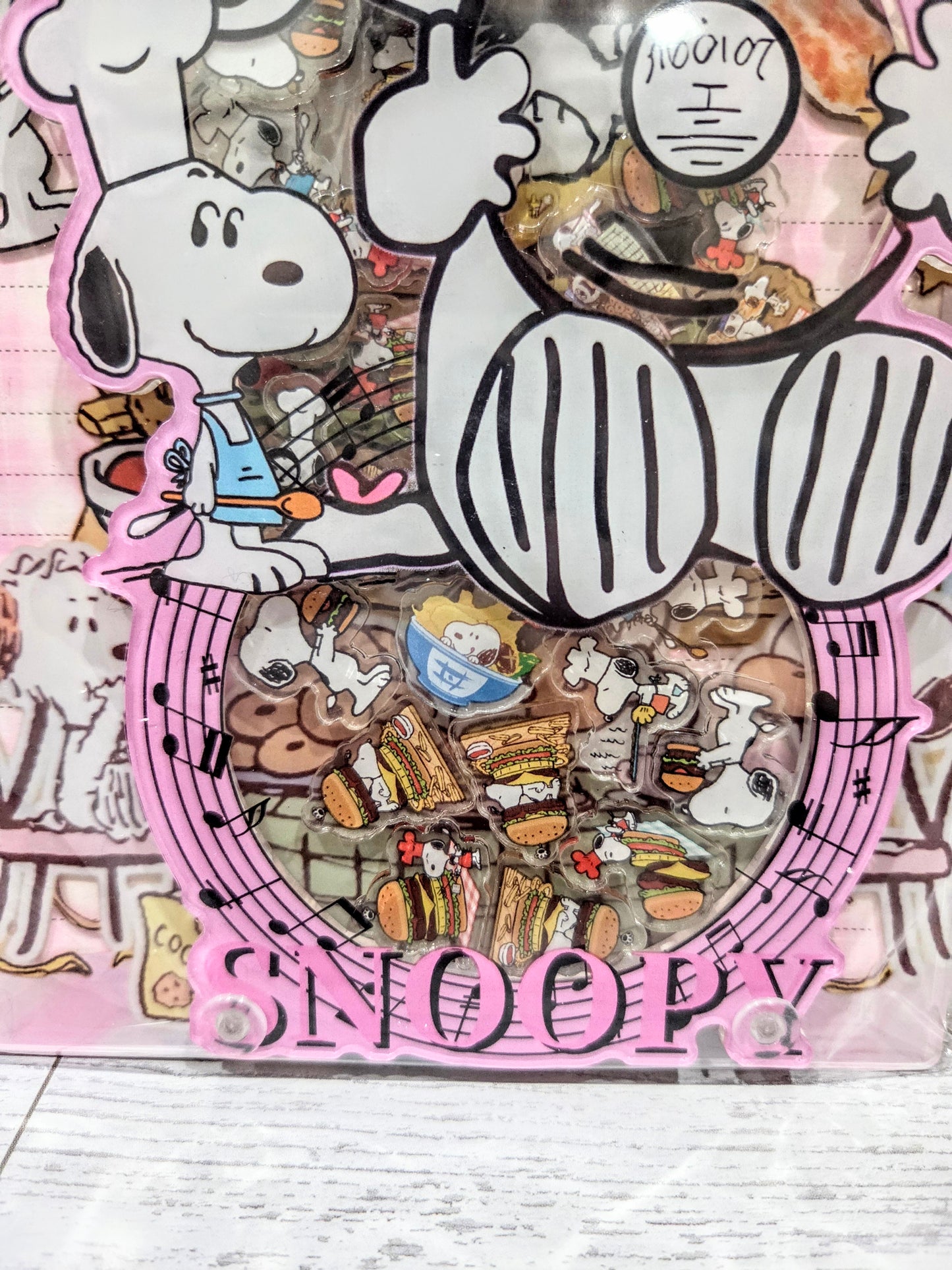 Close-up of A5 acrylic shaker notebook cover showing Snoopy chef, food icons, and pink border.