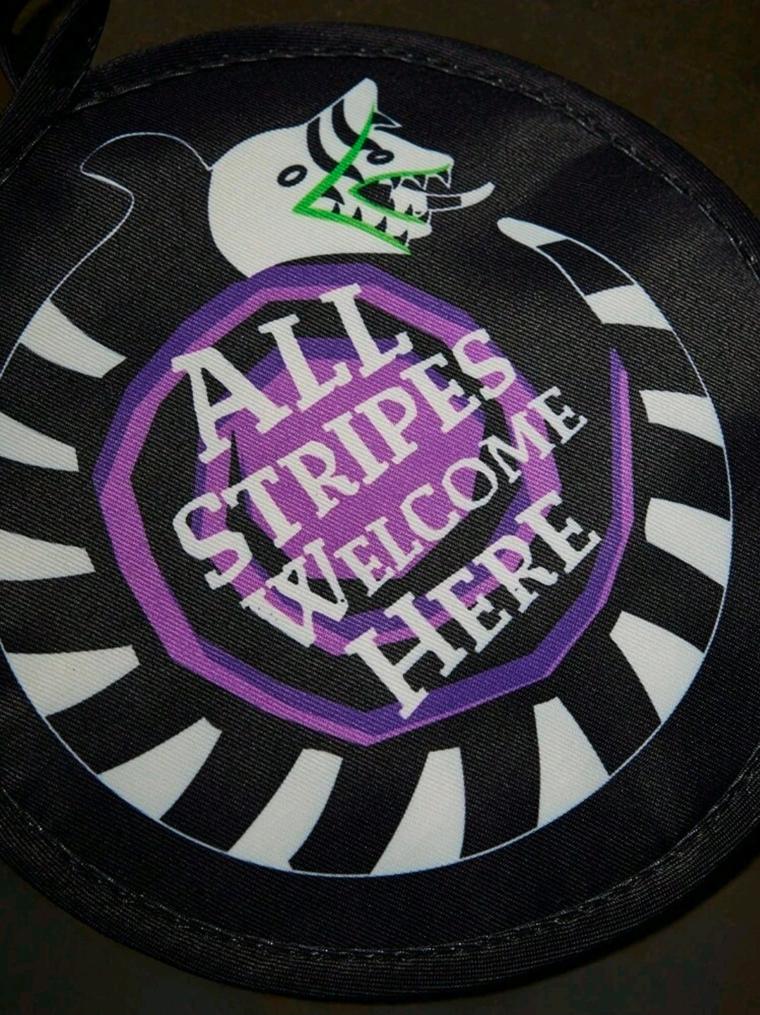 Round pot holder with black-and-white stripes and purple “All Stripes Welcome Here” text