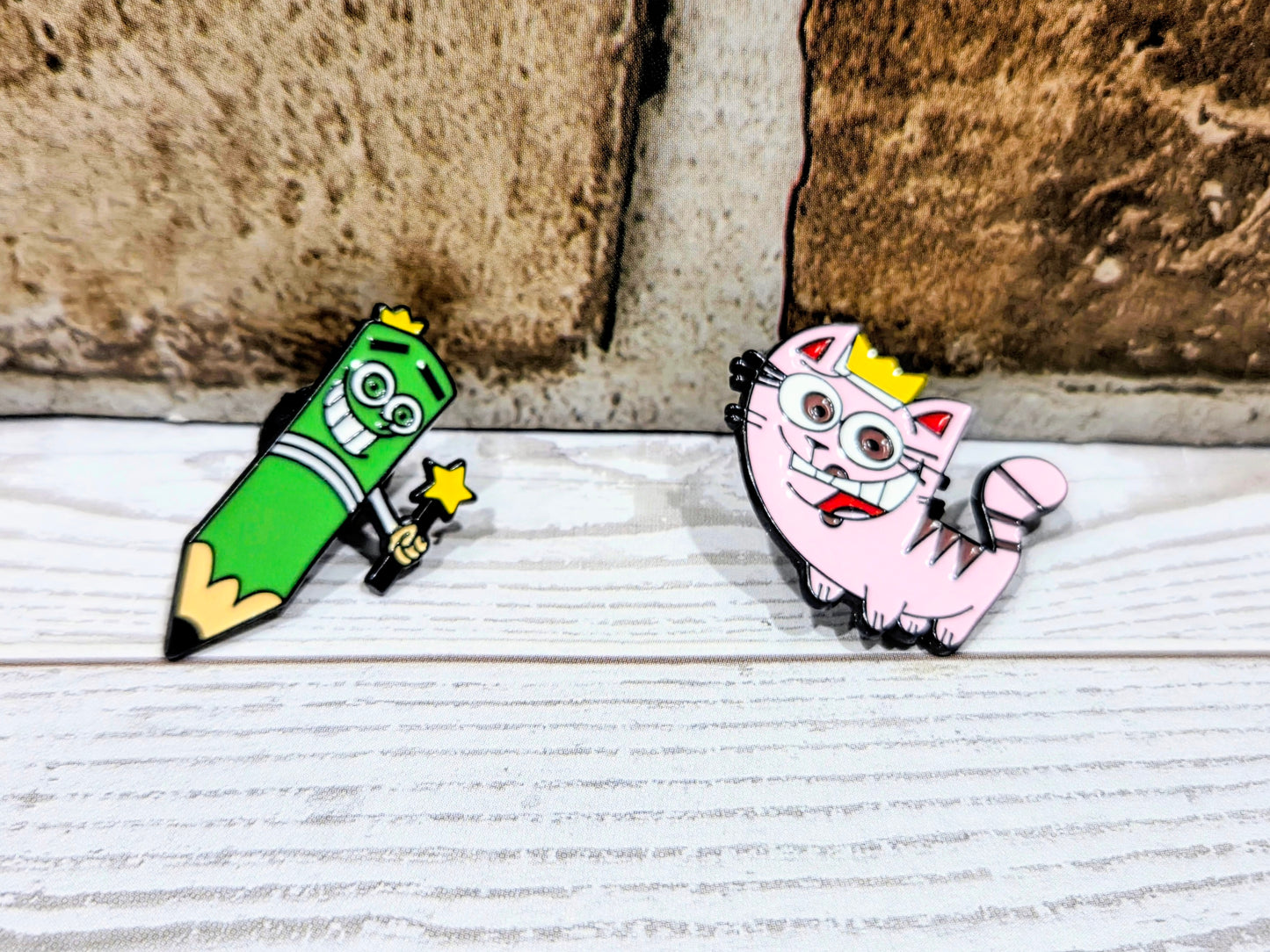 Two enamel character pins on a light surface: green cone and pink cone designs