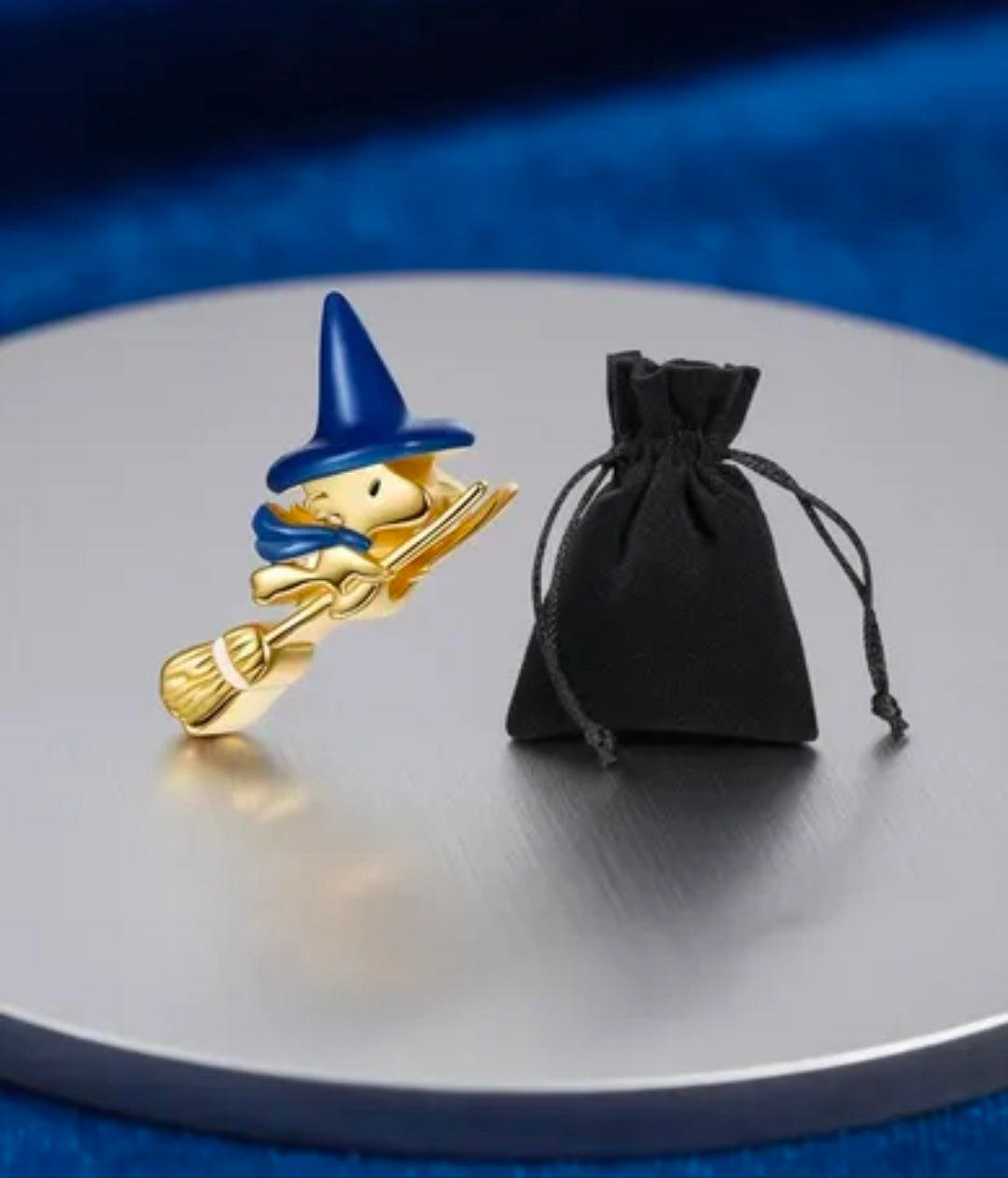 Gold-tone witch charm with blue hat and broom, paired with black pouch