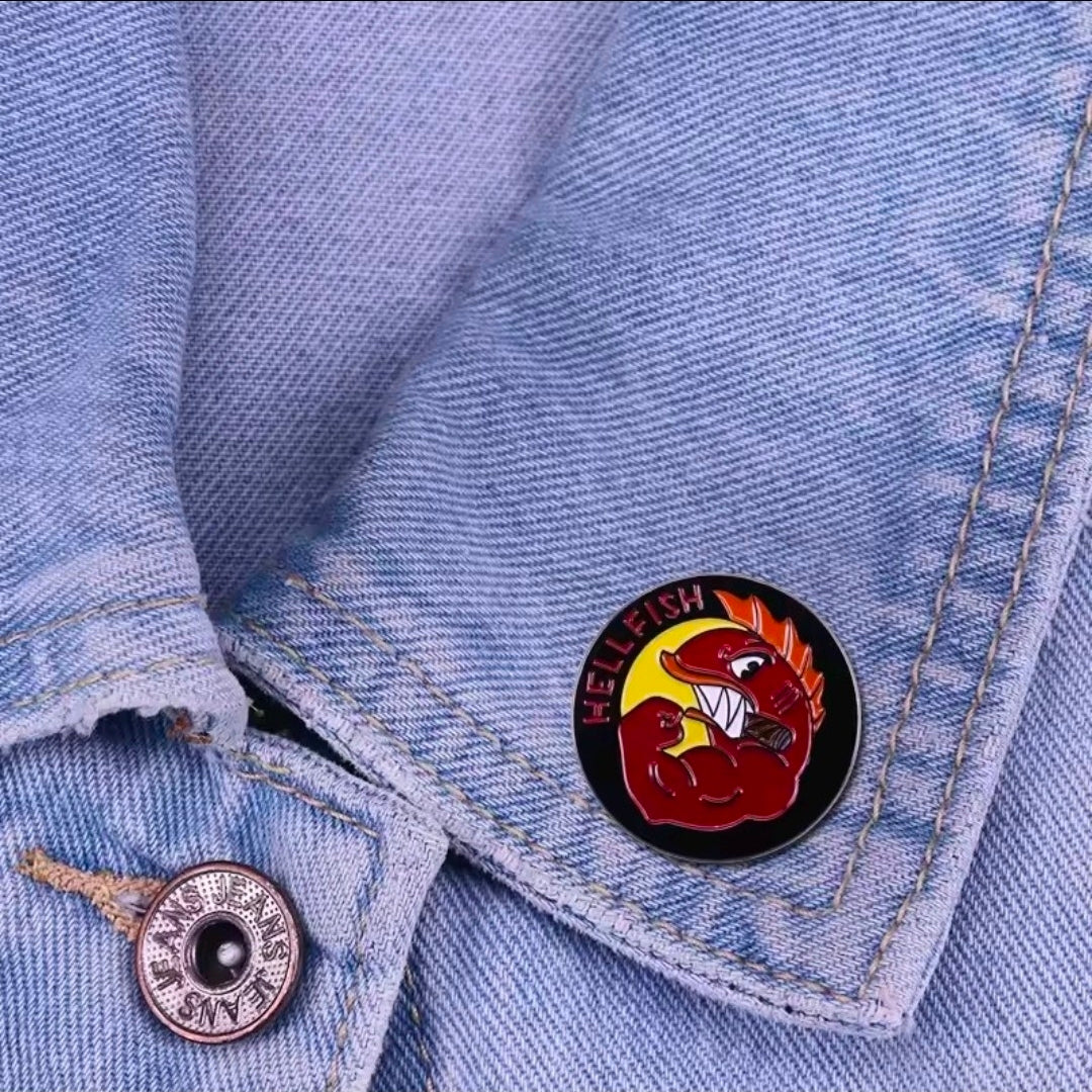 Round Hellfish enamel pin with red crab and black border on denim