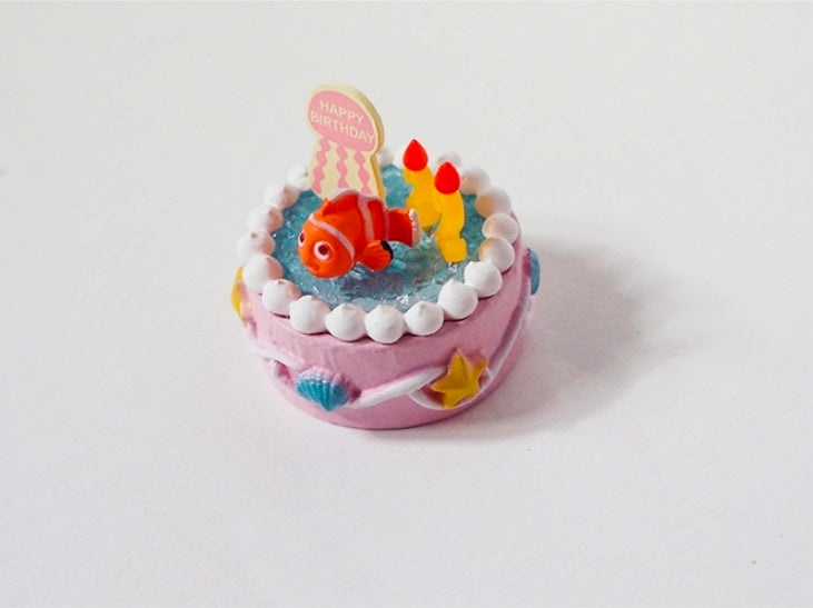 Birthday ocean cake mini figure with orange clownfish, candles, and “Happy Birthday” topper
