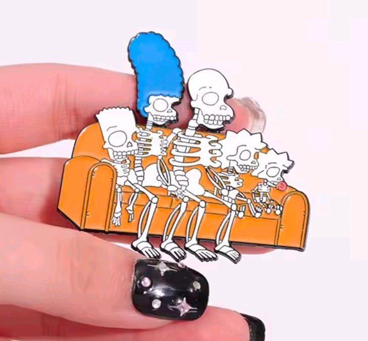 Skeleton couch enamel pin held in a finger, orange recliners and blue hair