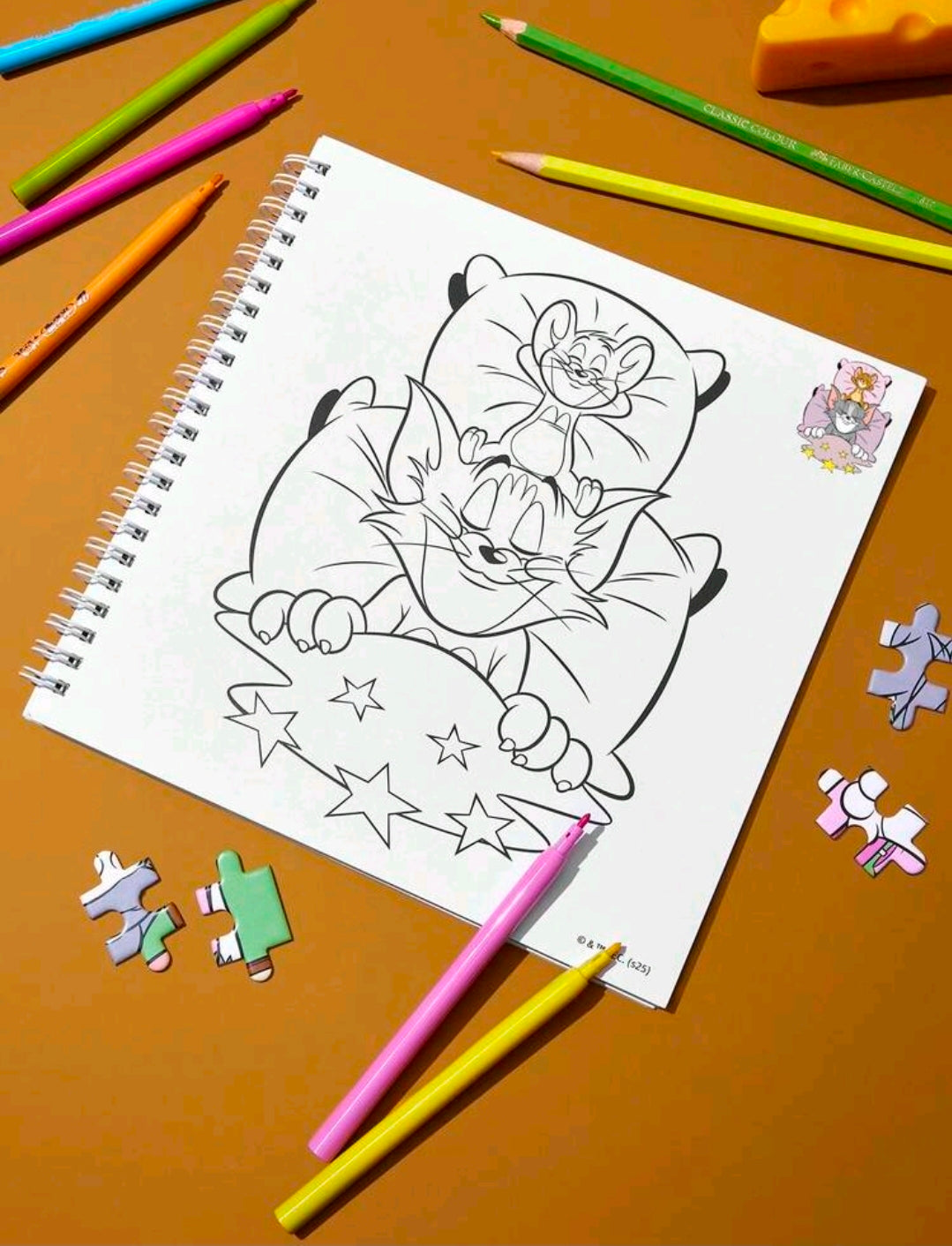 Spiral coloring book with black outline illustration of Tom and Jerry, pencils nearby