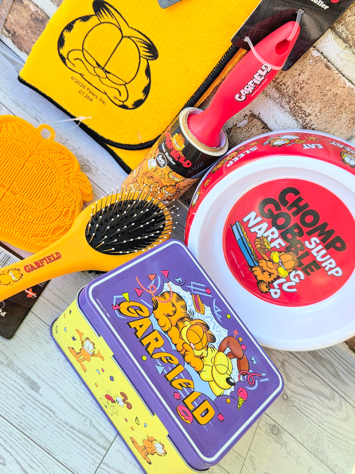 Garfield pet grooming set with red lint roller, brush, bowl lid, and purple tin.