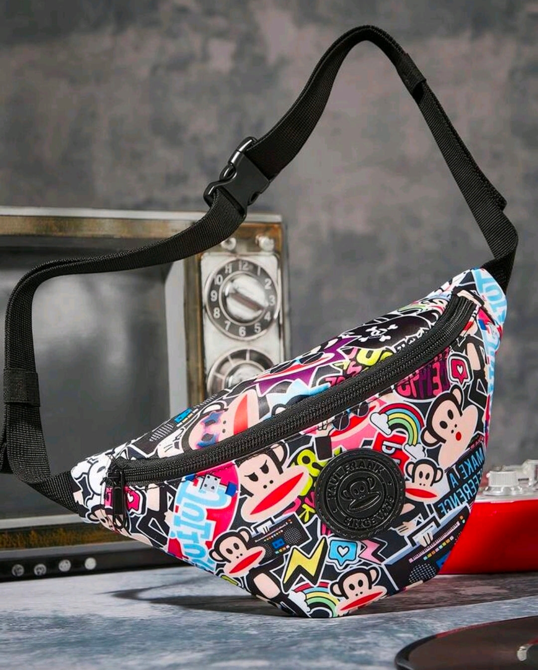 Side view of black belt bag with colorful sticker print and zipper pocket