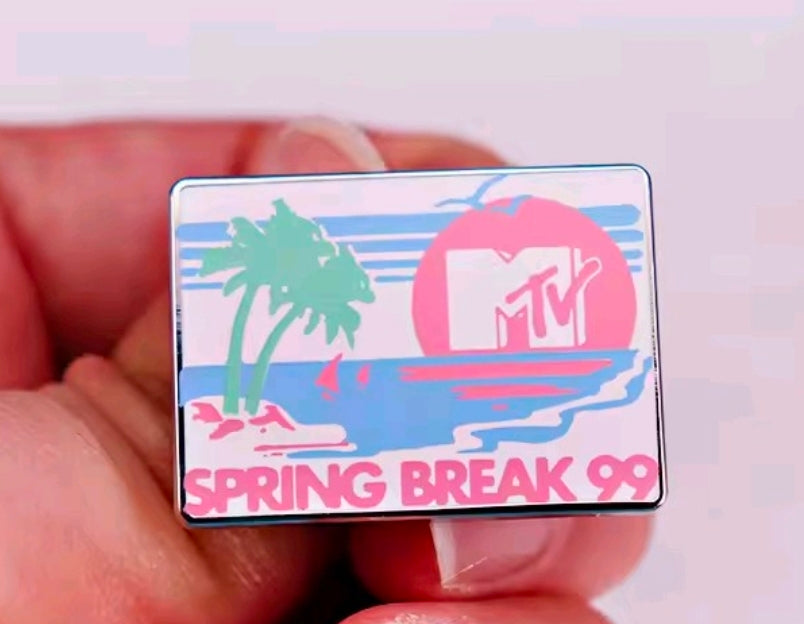 Spring Break 99 enamel pin held in hand, rectangular design with pink MTV circle and palms