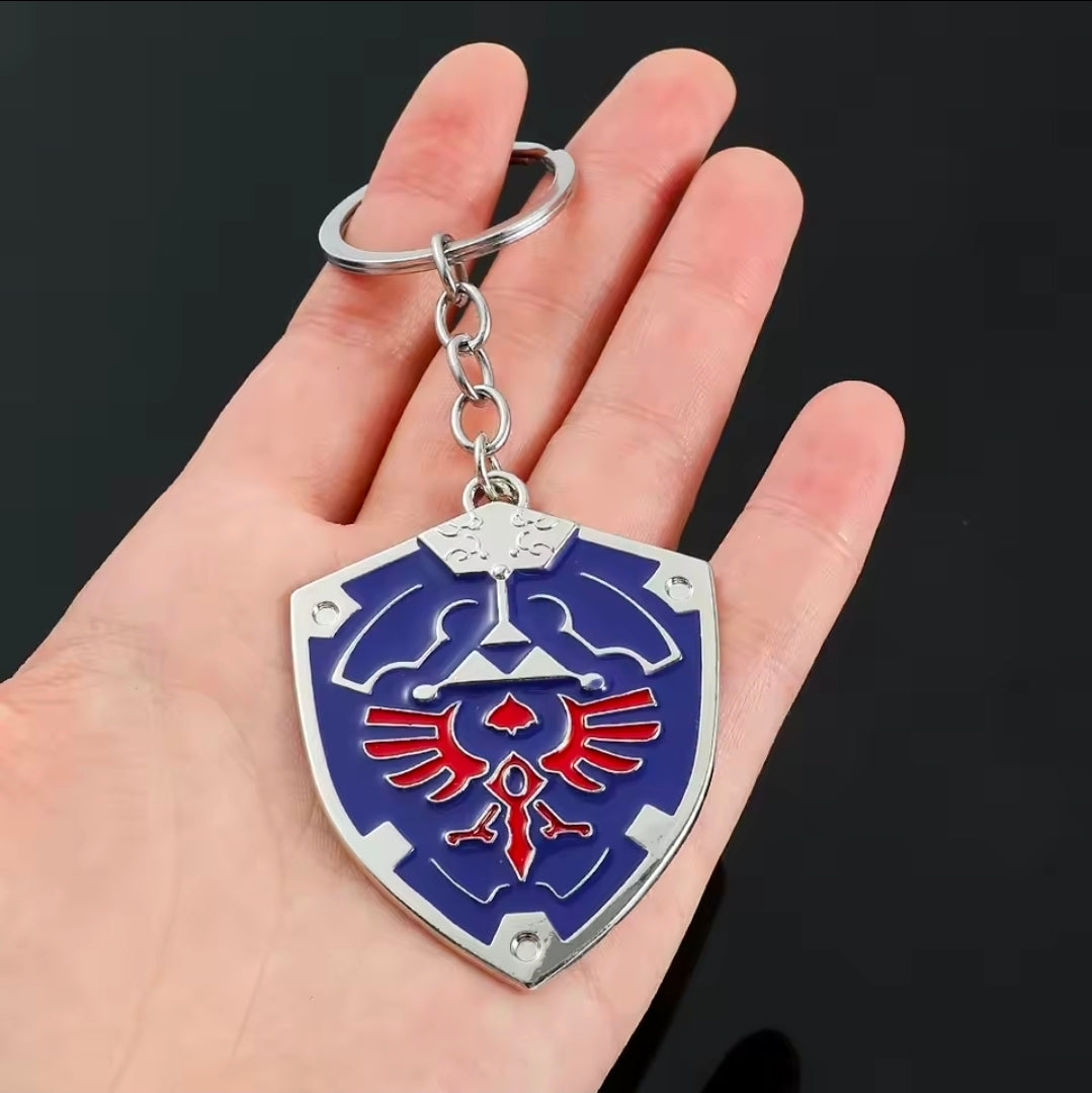 Blue metal enamel shield keychain with silver chain and split ring, held in palm