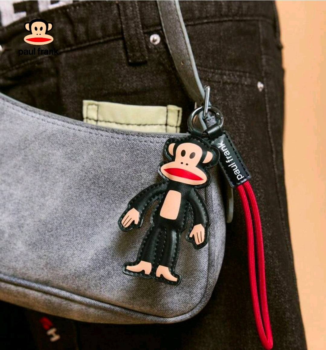 Julius monkey keychain bag charm on red lanyard attached to gray fabric bag
