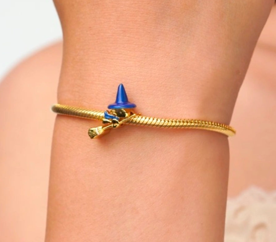 Gold-tone witch charm with blue pointed hat and broom, on snake chain bracelet