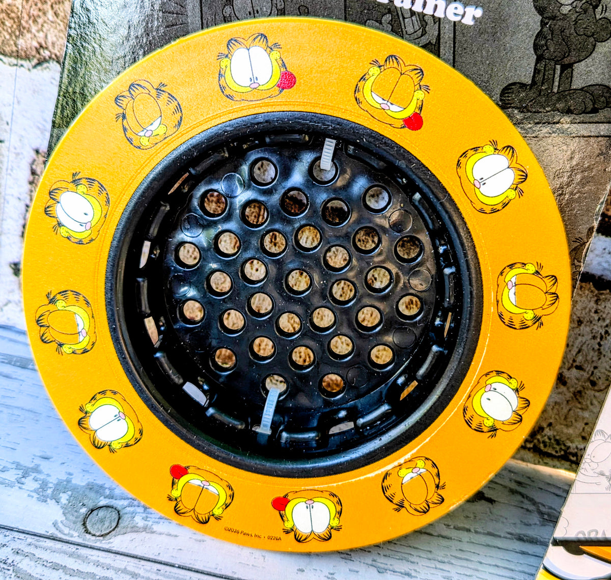 Yellow sink strainer with round black insert and Garfield character print