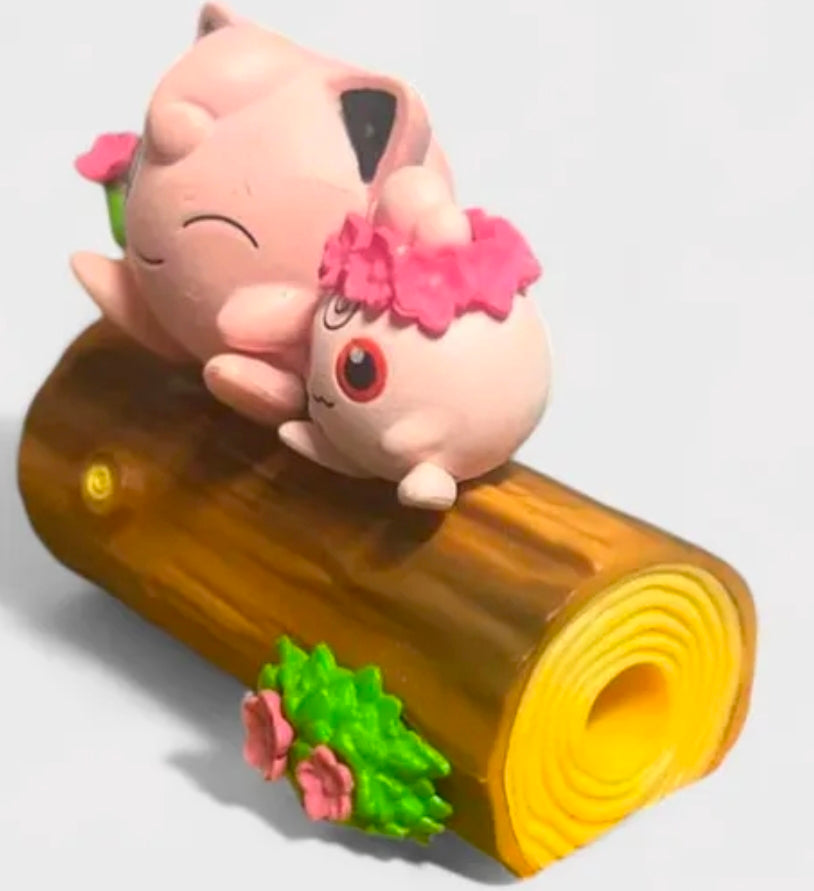 Pink toy figures hugging on a brown log with green leaves and a rolled log end.