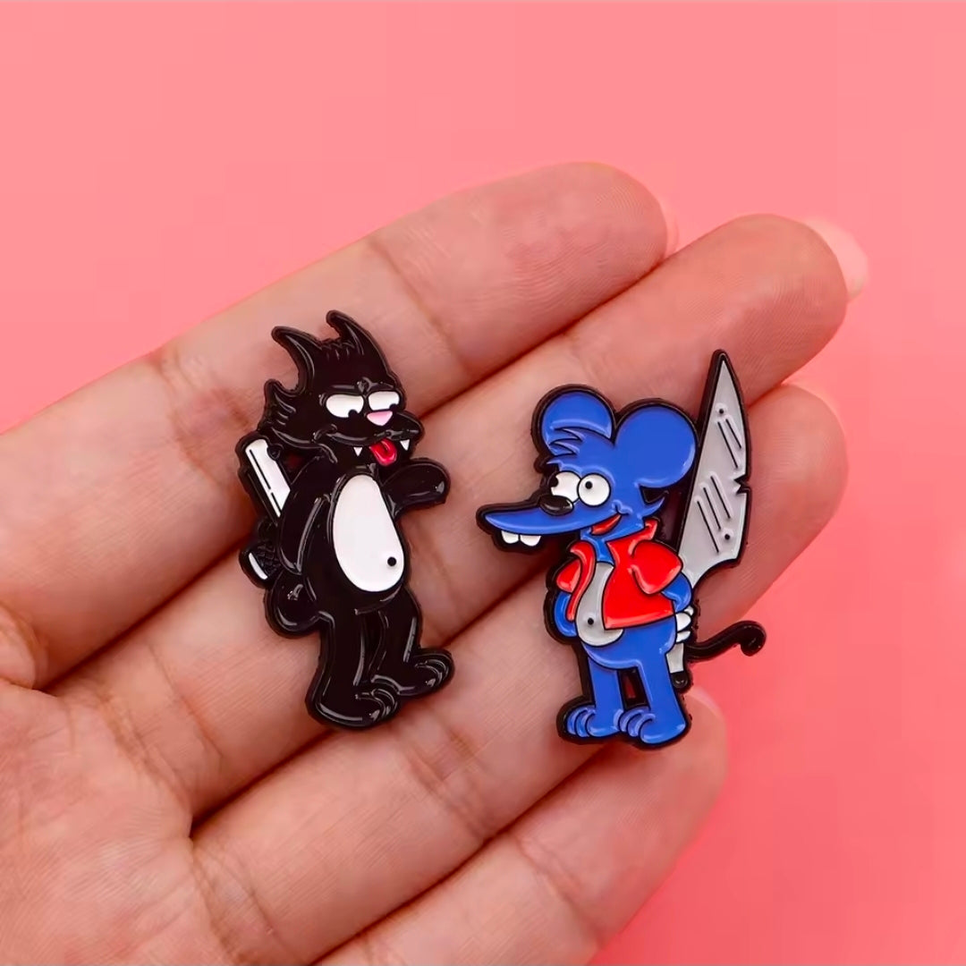 Two character enamel pins in hand: black cat and blue cat