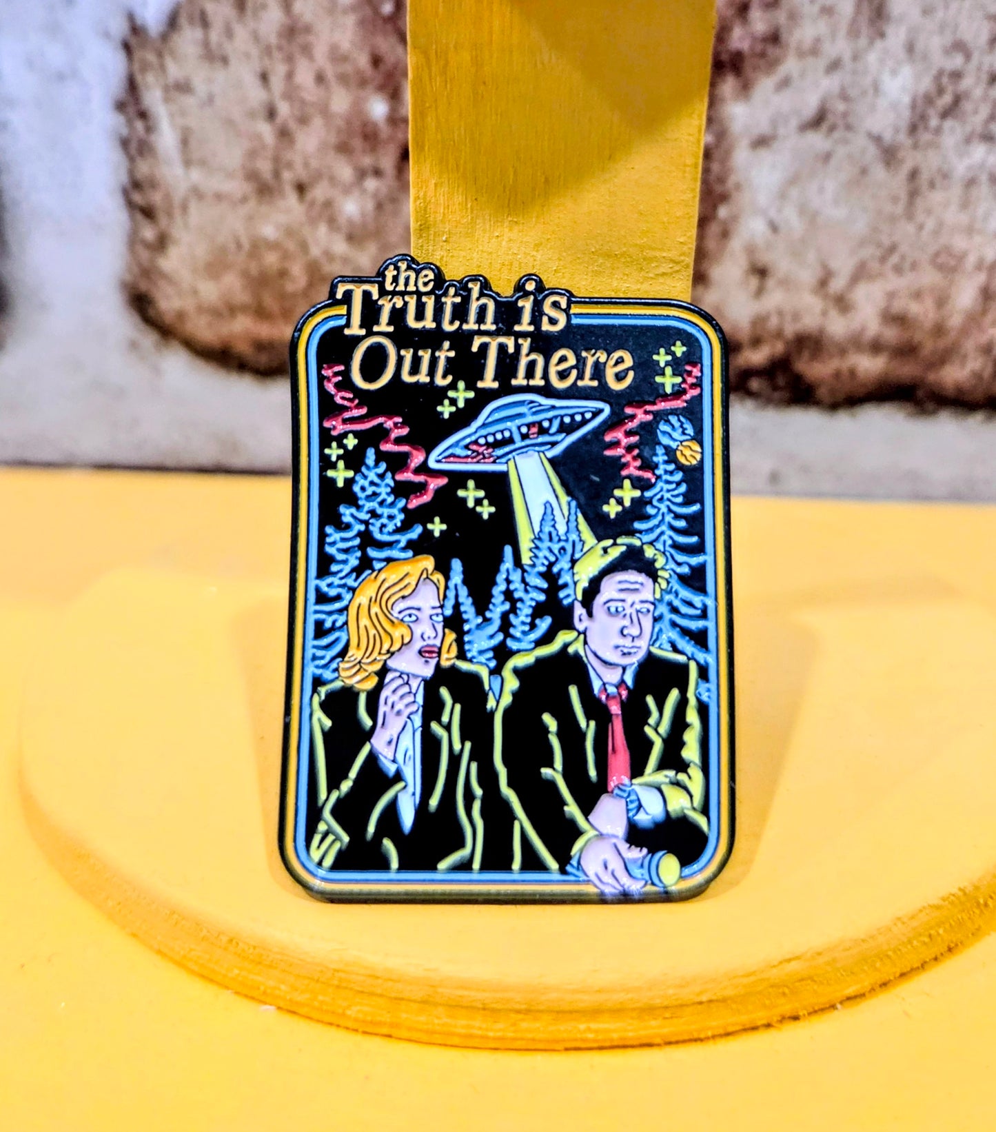 Square enamel pin with colorful “the Truth is Out There” scene and UFO artwork.