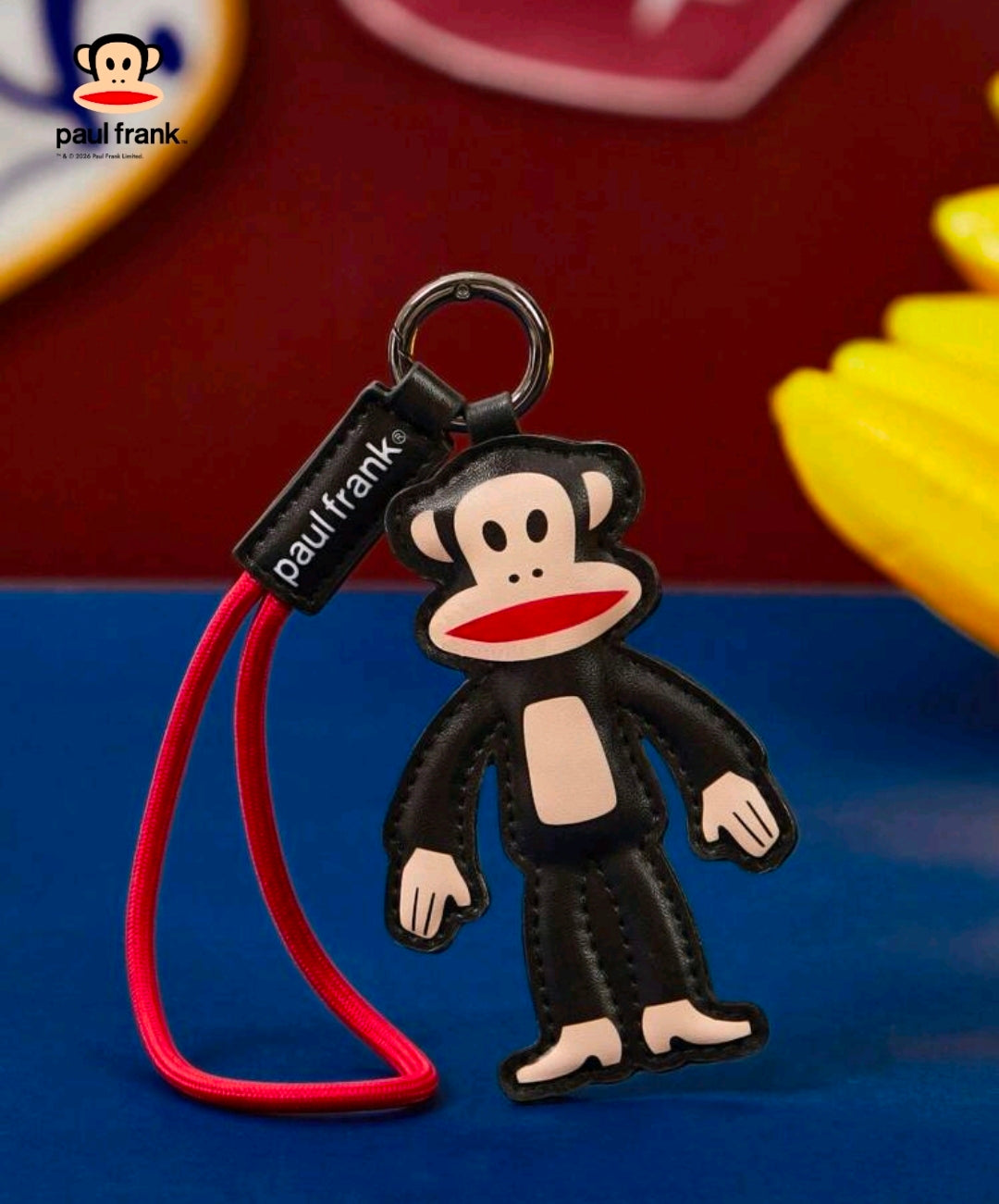 Julius monkey keychain charm with metal ring and black faux-leather tag on red cord