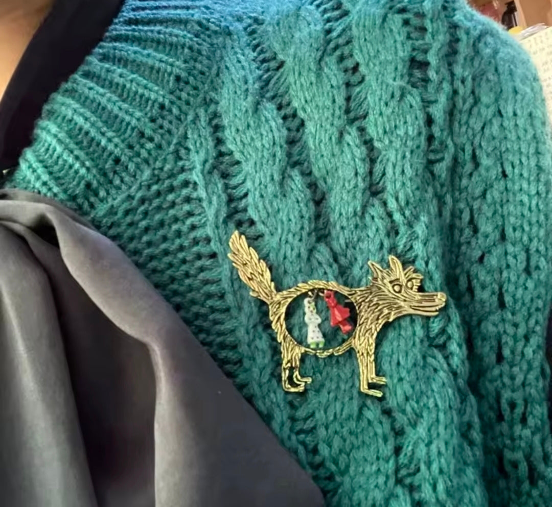 Gold-tone wolf brooch pin on teal knit: enamel wolf with circular Red Riding Hood charms.