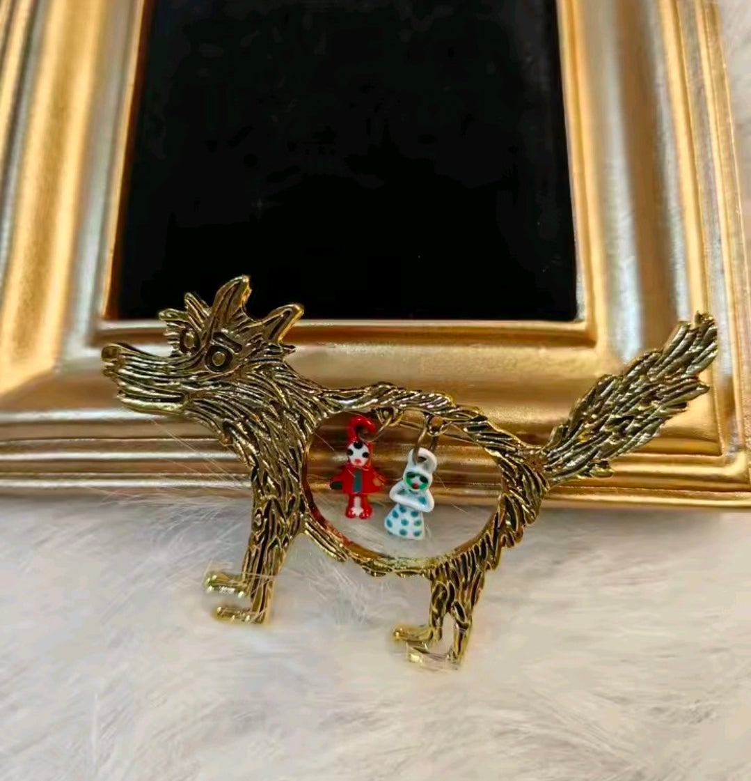 Gold-tone wolf brooch pin with circular Red Riding Hood and grandma charms on frame.