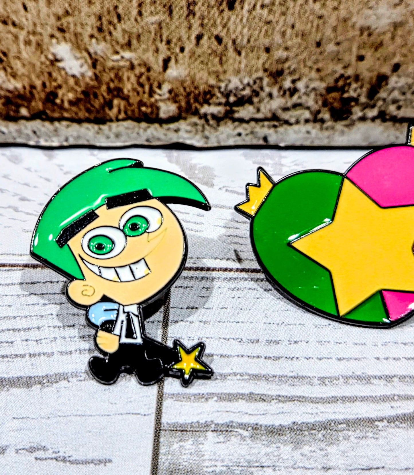 Enamel pin close-up of Timmy character with big eyes, green cap, and star charm.