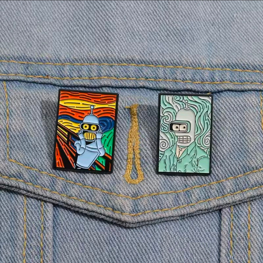 Two square enamel pins on denim: orange robot pin and teal robot pin