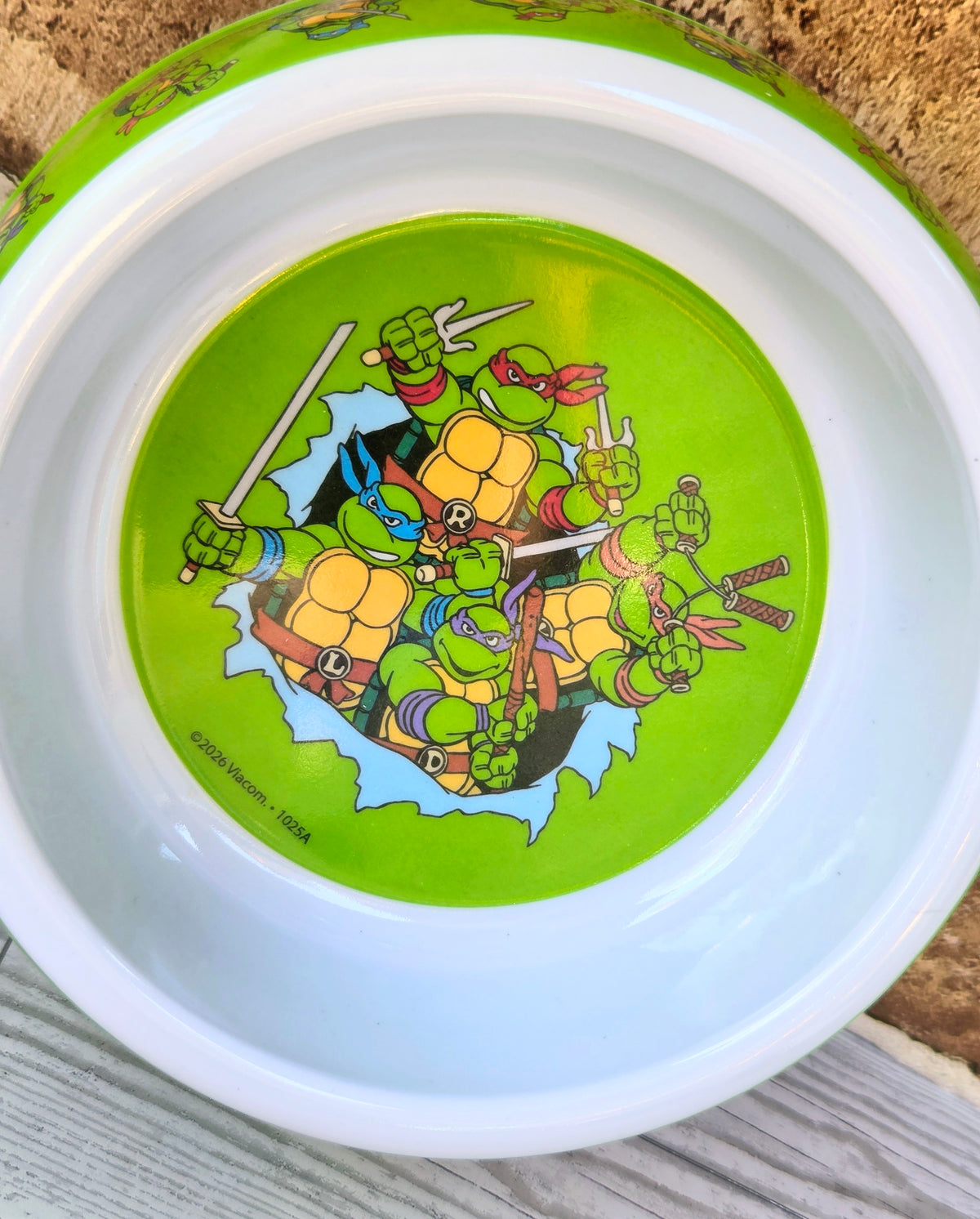 Bottom of neon green pet bowl with TMNT action-turtle illustration and brand mark
