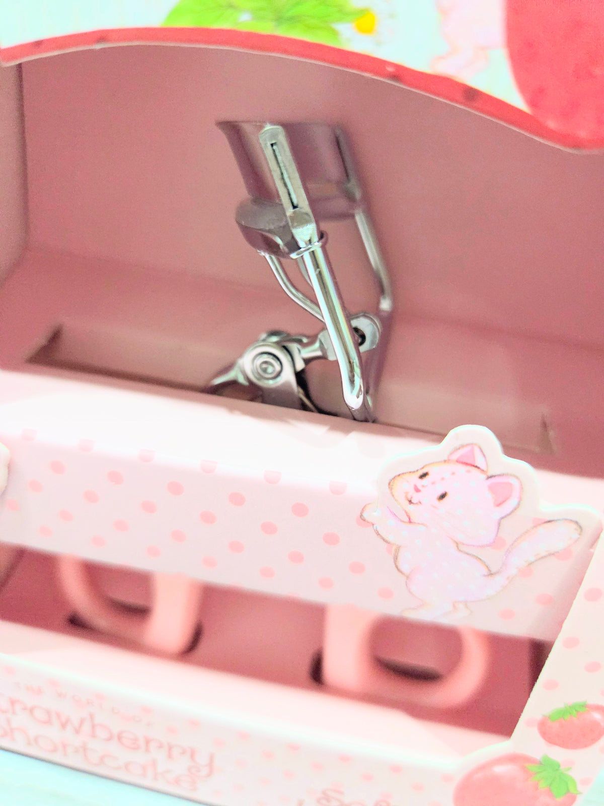 Pink strawberry eyelash curler with metal clamp inside open tray