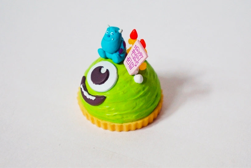 Green cupcake-style toy with Mike figure, red flame topper, and 'Happy birthday' card