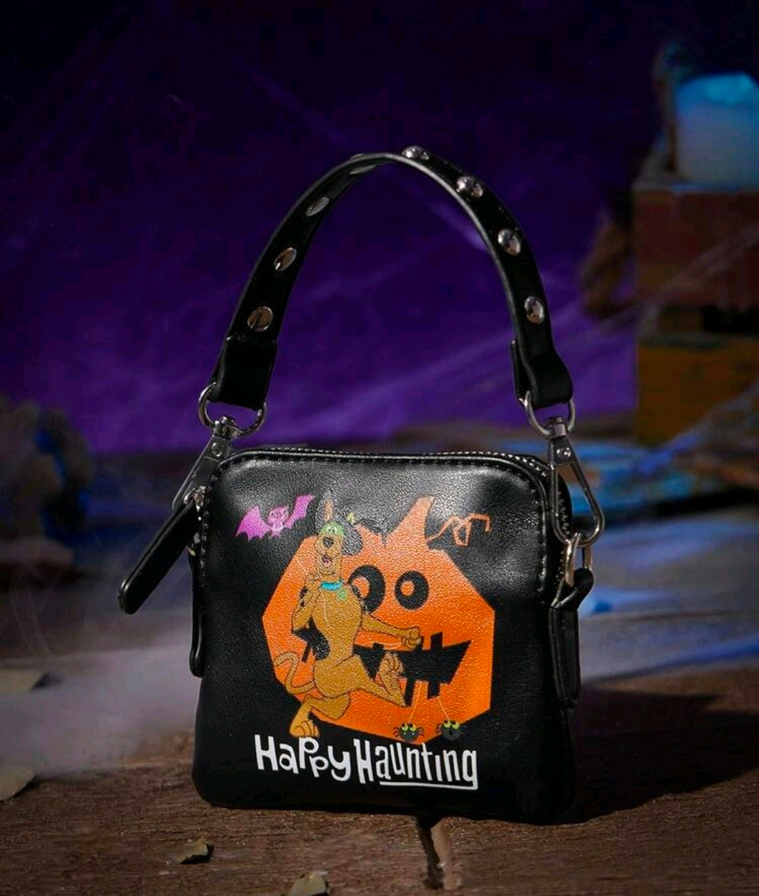 Black mini crossbody clutch with studded handle rings and Happy Haunting character graphic