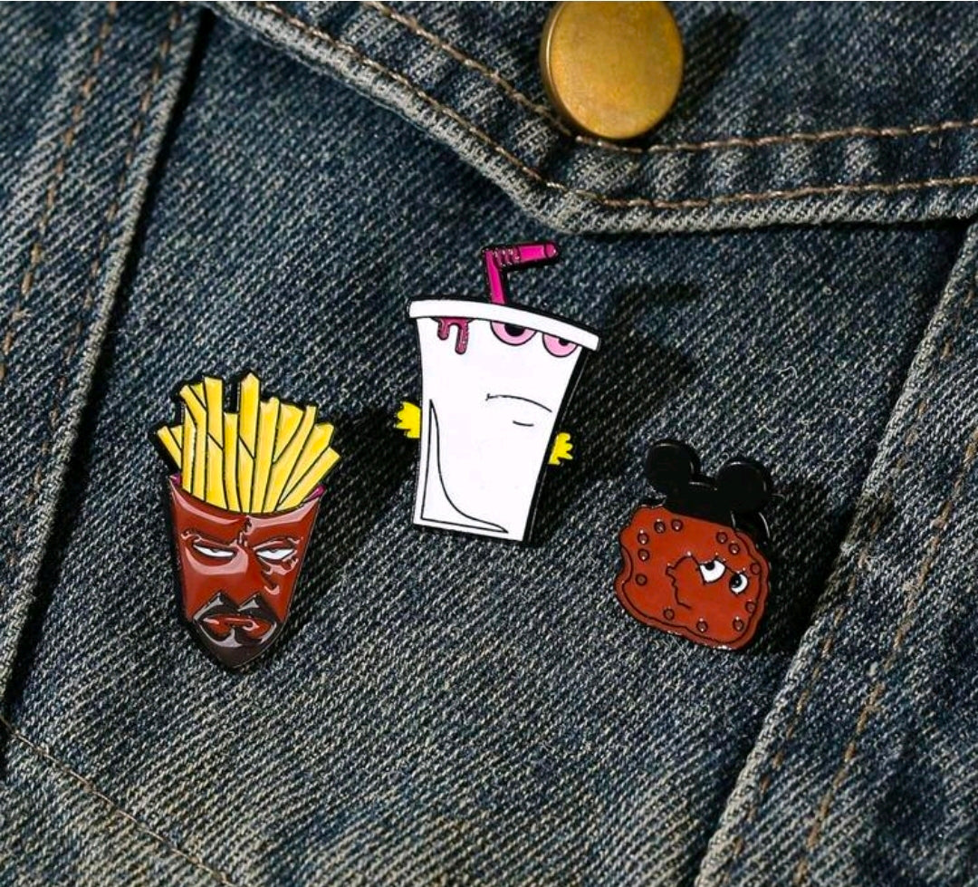 Enamel pin set on denim: white shake cup, fries face, red cookie with black ears