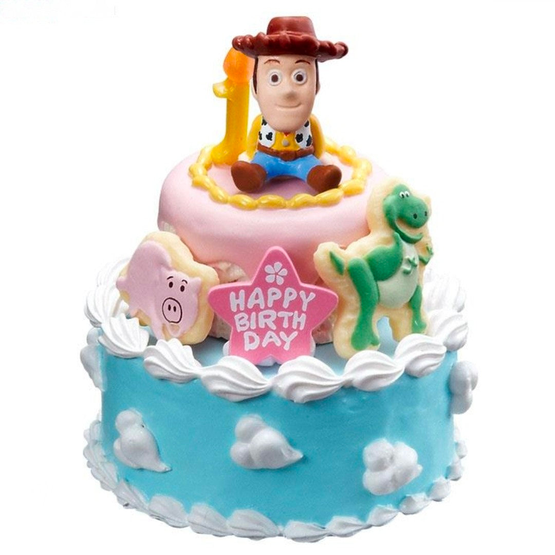 Close-up mini birthday cake toy with Woody figure, pink top, “Happy Birthday” banner, blue sides