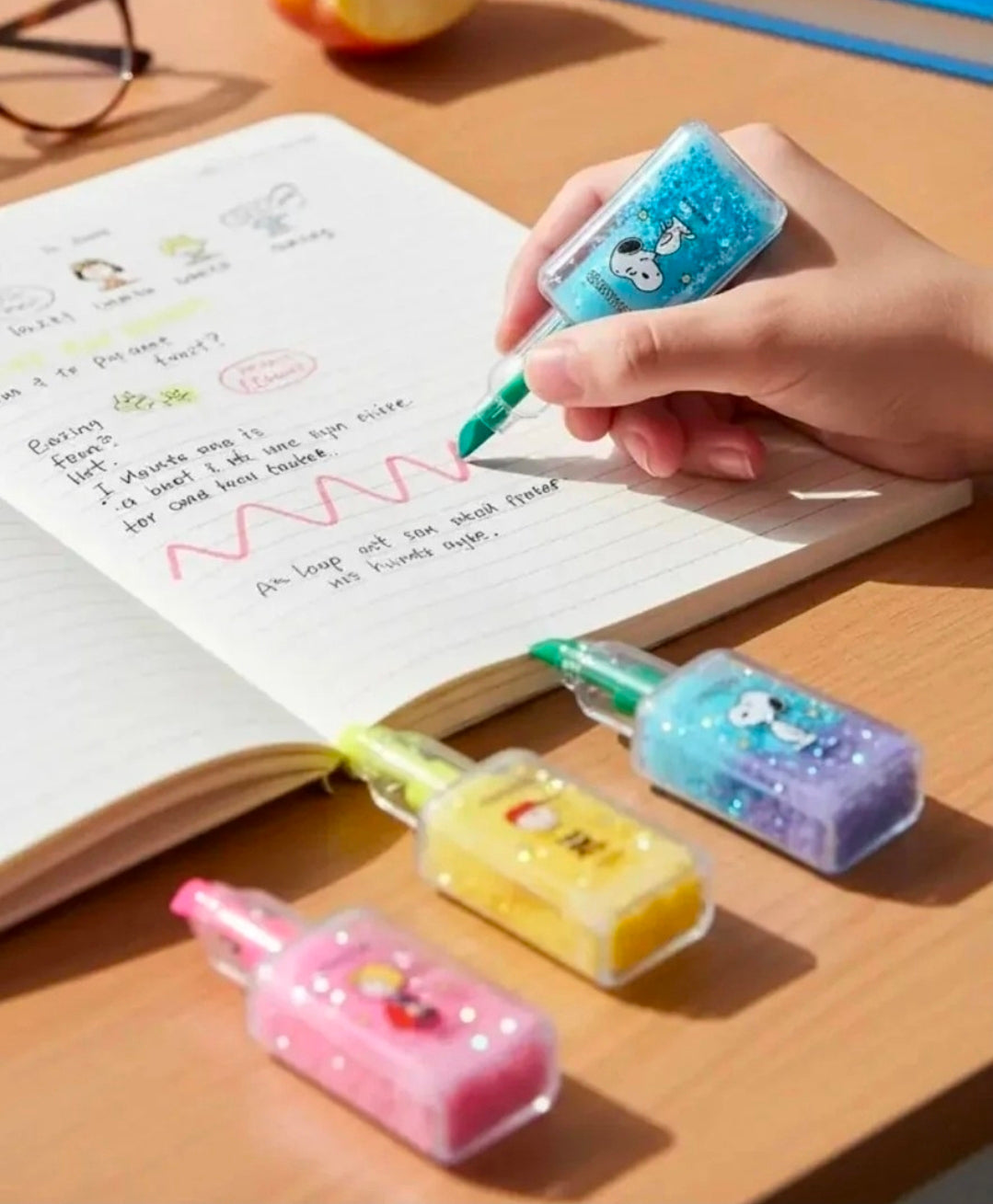 Peanuts glitter highlighter bottles held while writing in a notebook.