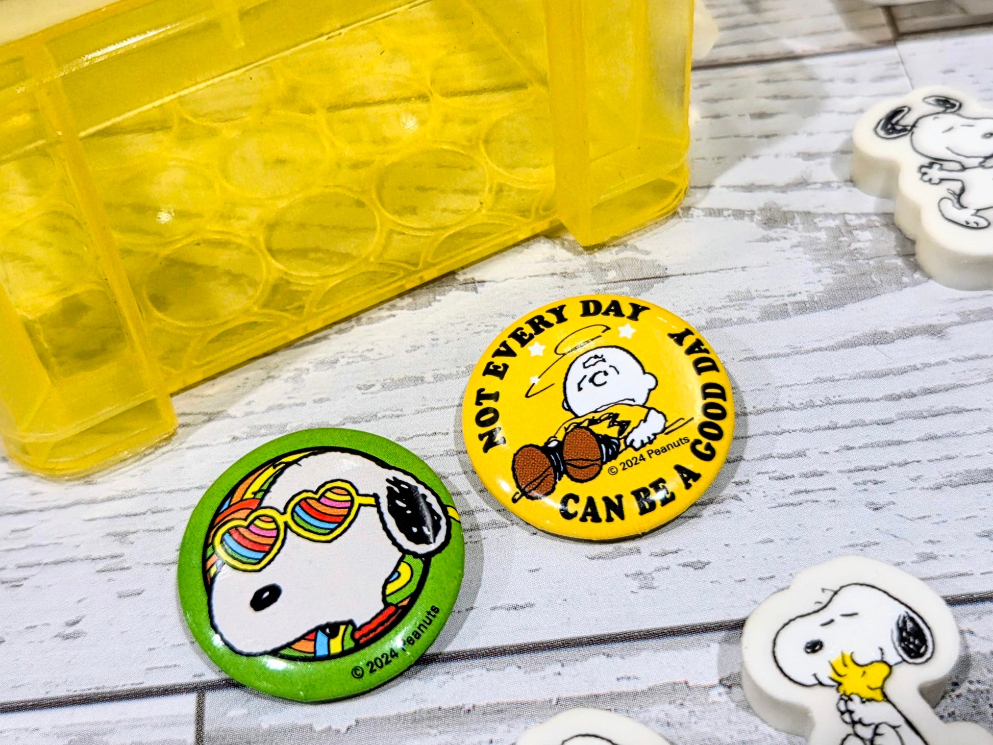 Yellow desktop organizer box with Snoopy-themed round badge pins and small erasers