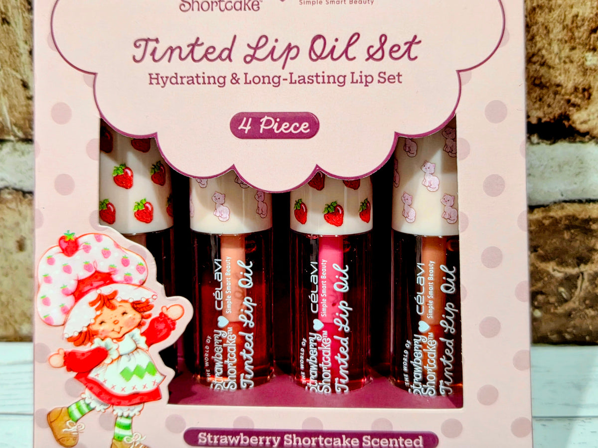 Four tinted lip oil bottles in open gift set holder, Strawberry Shortcake branding visible.
