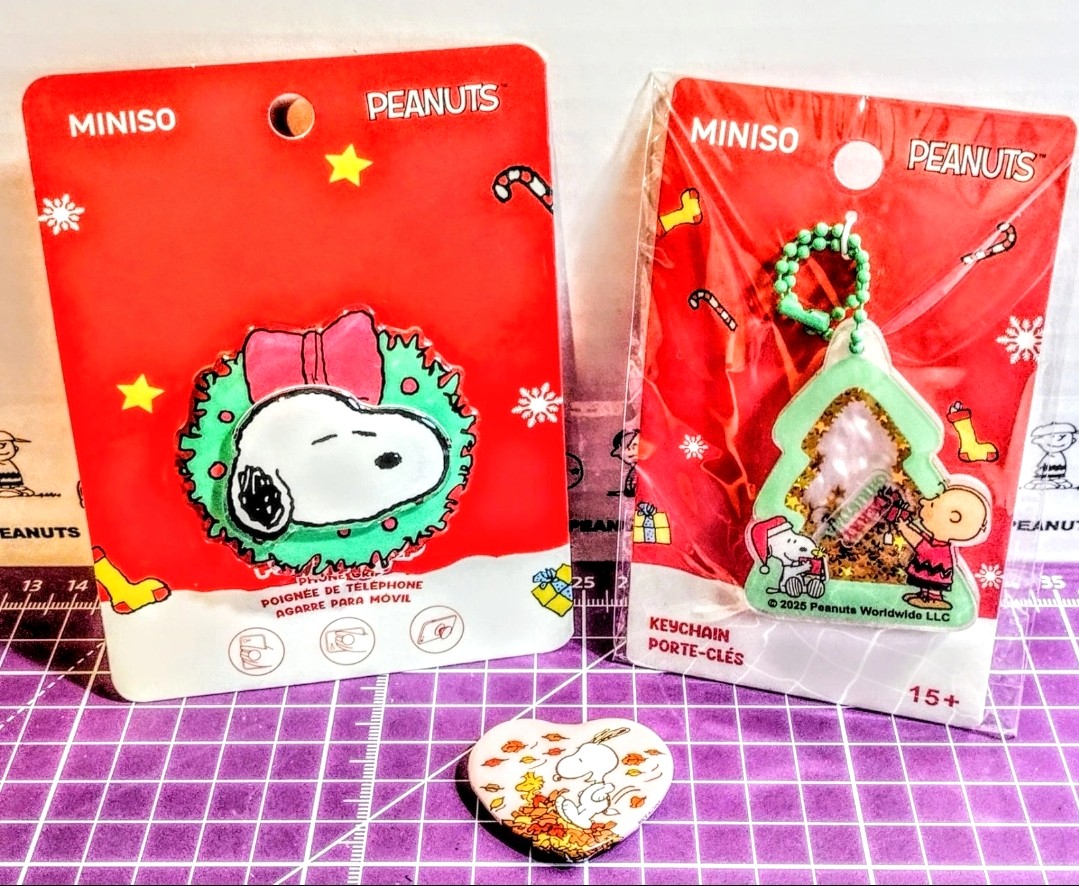 Two red MINISO PEANUTS blister cards showing Snoopy keychain charm and phone grip piece.