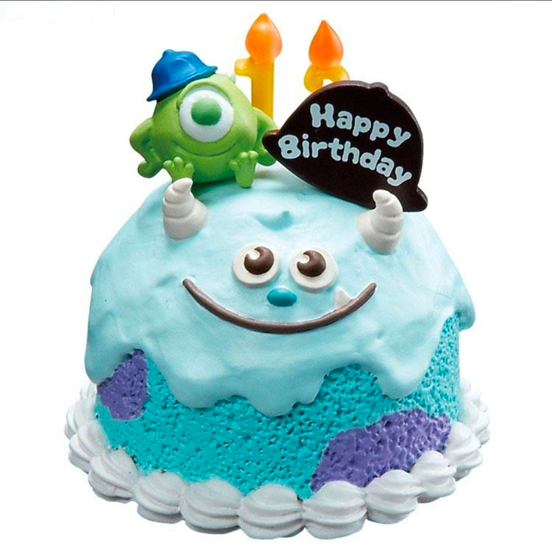 Close-up mini birthday tart figure with two candles, smiling face, and Happy Birthday plaque