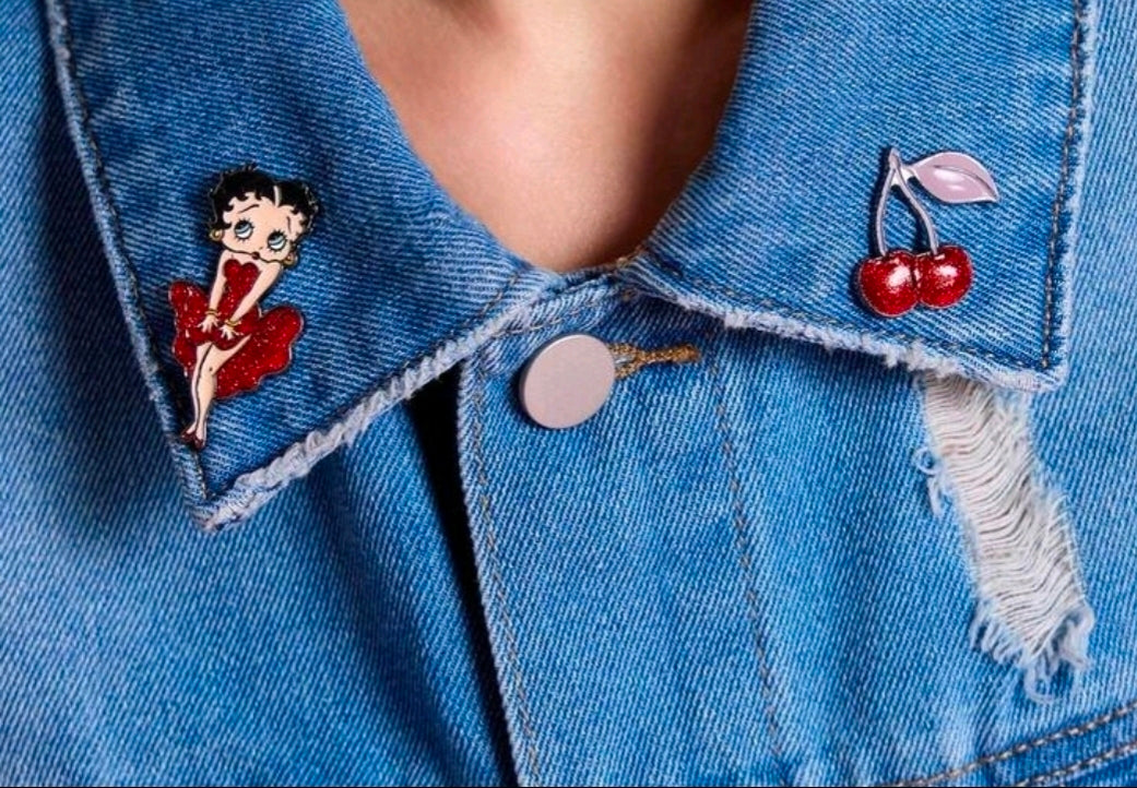 Betty Boop enamel pin and red cherries enamel pin on blue denim jacket lapel