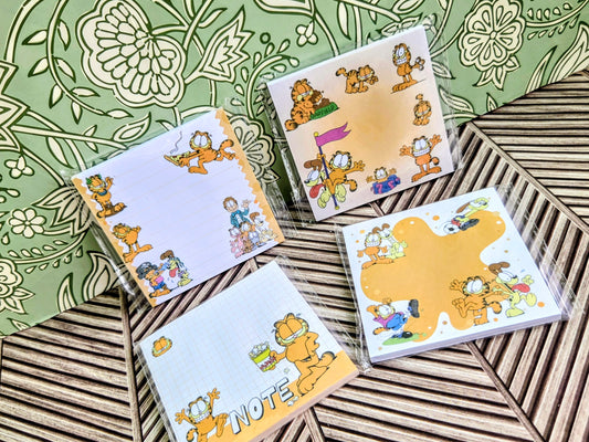 Set of four Garfield sticky note pads with cartoon scenes on orange and white covers